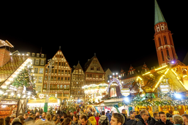 Ein geschäftiger Weihnachtsmarkt in Nürnberg, Deutschland mit Menschen um geschmückte Stände, festliche Lichter, Gebäude mit Fenstern und einen Kirchturm unter einem dunklen Himmel.