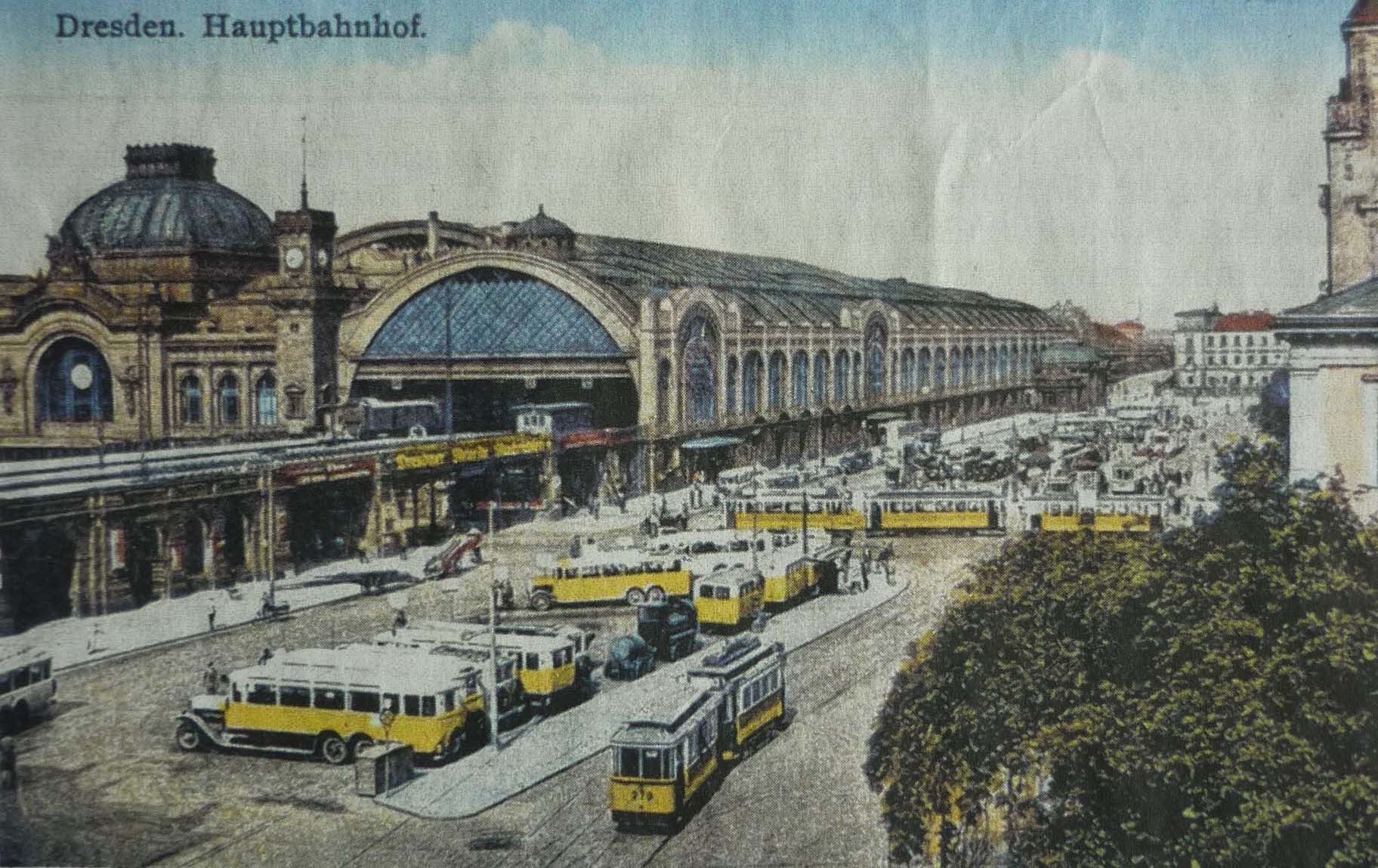 Schwarze und weiße Postkarte des Dresdner Hauptbahnhofes: Eine belebte Straßen Szene mit Fahrzeugen, Fußgängern, Bäumen, Gebäuden und einem bewölkten Himmel.