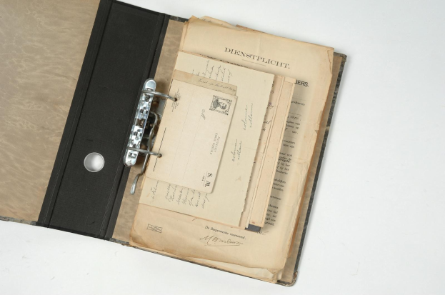 Ein alter schwarzer Ordner voller Papiere, wahrscheinlich deutsche Militärdokumente, auf einer weißen Oberfläche.