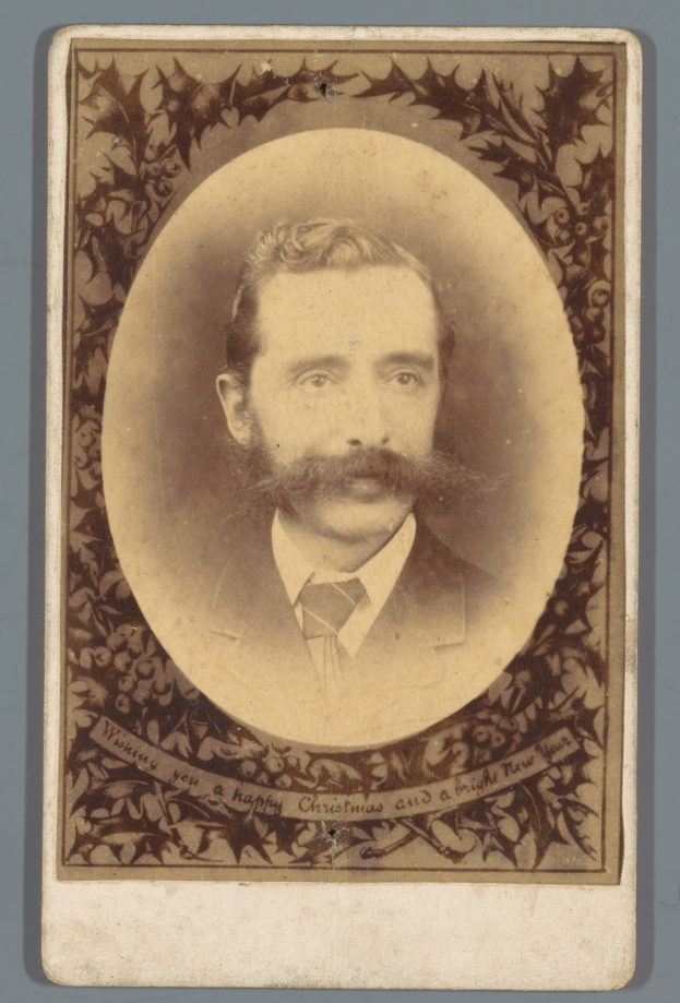 Ein altes Foto eines Mannes mit Schnurrbart und Bart, der direkt in die Kamera schaut und ernst dreinschaut.