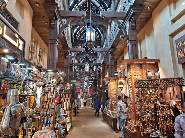 Ein belebter Dubai-Basar mit Menschen, die zwischen Warenregalen hindurchgehen, beleuchtet von Deckenlampen und mit Texttafeln an den Wänden.