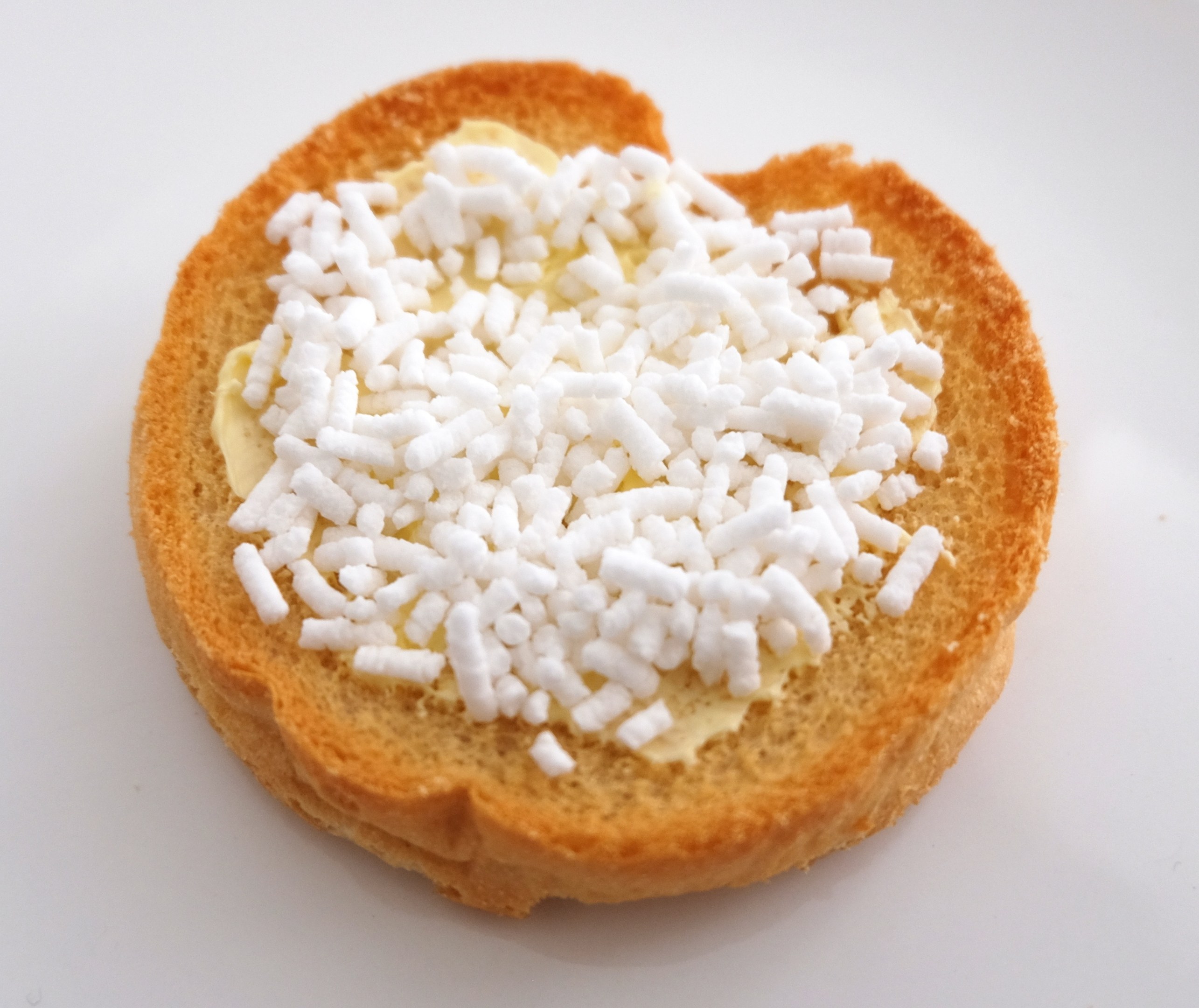 Herzförmiges Brotscheibchen mit Butter und weißem Zucker auf einer weißen Oberfläche.