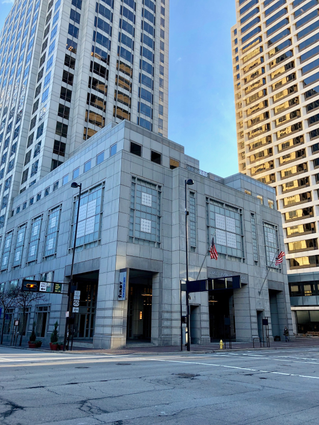 Großes Gebäude mit vielen Fenstern, identifiziert als Hauptquartier der Chicago Public Library, auf einer Stadtstraße mit Straßenmöbeln, Bäumen und einem bewölkten Himmel.