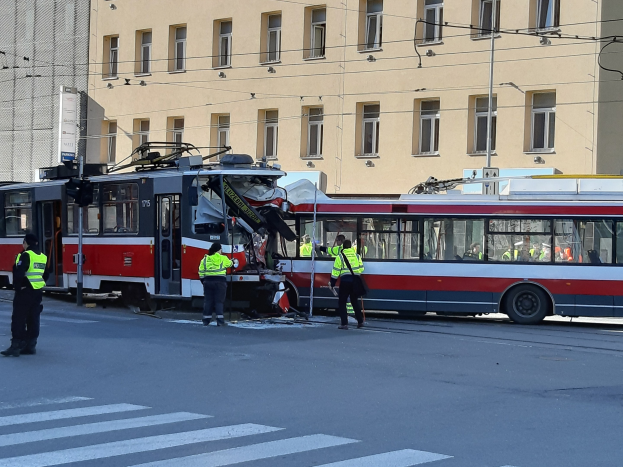 Rote und weiße Tram bei einem Unfall an der Straße mit Menschen in der Nähe und einem Gebäude im Hintergrund.