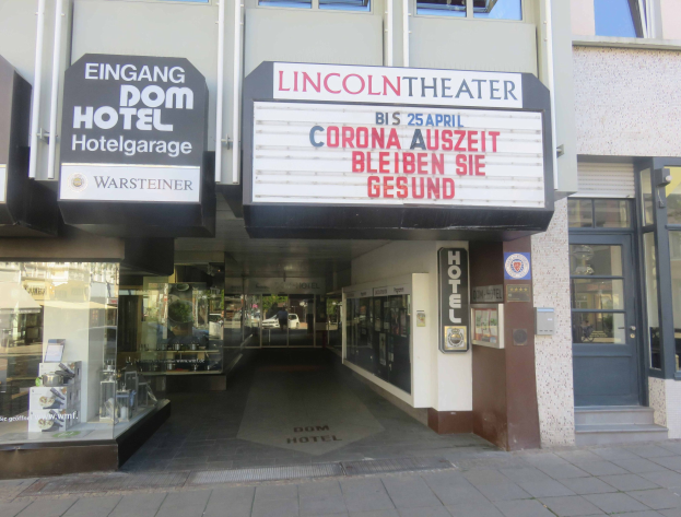 Außenansicht des Lincoln Theaters in Berlin, Deutschland, mit Glasfenstern und -türen und einer Tafel sowie einem Innenraum, der eine pulsierende Stadtlandschaft vermuten lässt.