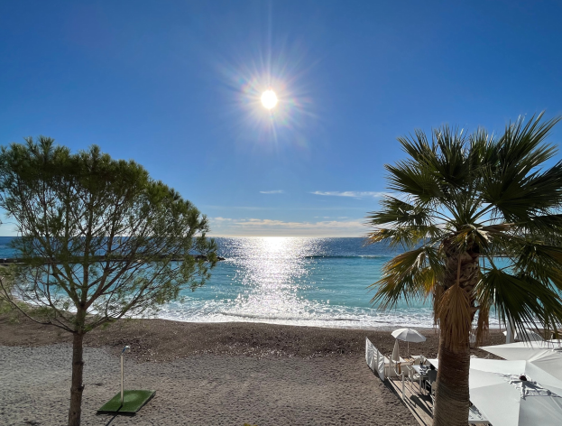 Ein sonniger Strand mit Palmen, Sonnenschirmen und üppiger Vegetation an der französischen Riviera.