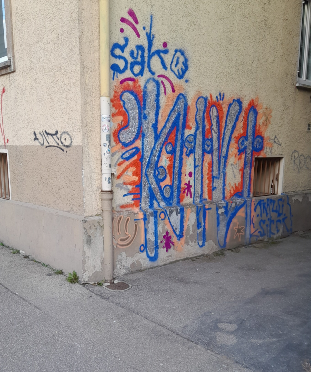 Ein Gebäude mit Fenstern, einem Rohr und Graffiti an der Seite, das über einer Straße liegt.