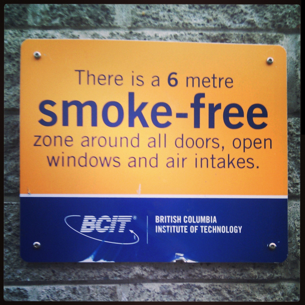 Ein Schild an einer Wand, das eine 6 Meter rauchfreie Zone um Türen, offene Fenster und Luftansaugöffnungen anzeigt.