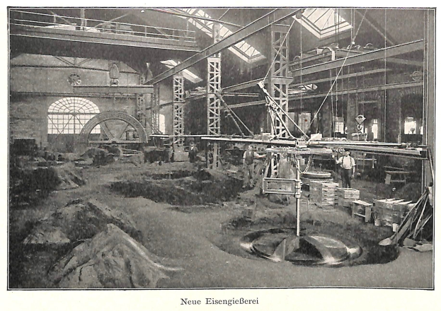 Schwarzes und weißes Foto einer Fabrik mit Arbeitern, die Maschinen bedienen, umgeben von Metallstangen und Pfählen; Text unten lautet "Neue Eisenglebeerei, die erste Fabrik in Deutschland".