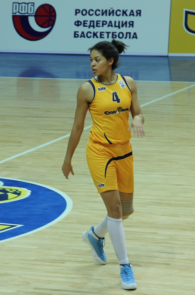 Ein professioneller Basketballspieler in einem gelben Trikot dribbelt auf einem Feld mit einer Tafel im Hintergrund.