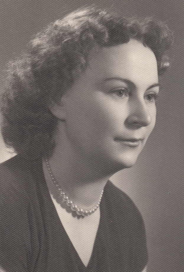 Ein Schwarz-Weiß-Foto einer Frau mit ernster Miene, die eine Kette trägt und ein einfaches Kleid mit hohem Kragen und langen Ärmeln trägt, ihr Haar ist zurückgekämmt und ihre Augen sind fokussiert.