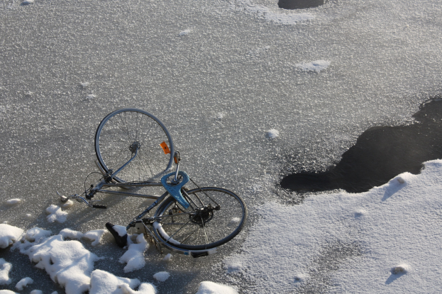 Ein Fahrrad liegt im Schnee neben einer Wasserlache, umgeben von einer Schneedecke.