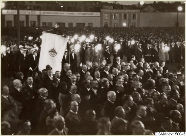 Schwarzes und weißes Foto einer großen Menge vor einem Gebäude, mit einer Person, die eine Flagge hält, Polen und Lichter im Hintergrund und Text unten, der "Gustav Klimts Rede an der Berliner Mauer" lautet.