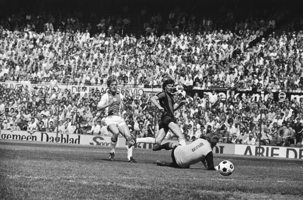 Schwarzes und weißes Foto von Männern, die auf einem Feld Fußball spielen, mit Zuschauern im Hintergrund und einem Banner "Bundesliga 1978-79 Ajax 1-1 Hannover 96"