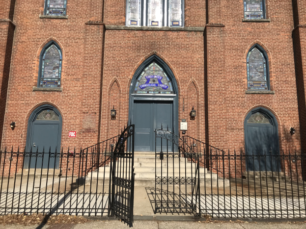Außenansicht der Ersten Vereinigten Evangelischen Kirche in Chicago, mit einem großen Backsteingebäude mit einem schwarzen Tor, Fenstern, Türen, Treppen, Geländern, Lampen und einer Straße davor.
