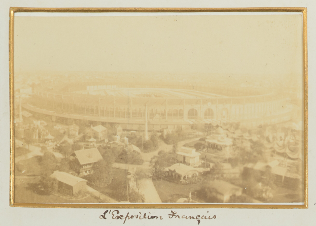 Altes Schwarz-Weiß-Foto eines Stadions, umgeben von Stadtgebäuden, Bäumen und Strommasten, mit Text am unteren Rand.