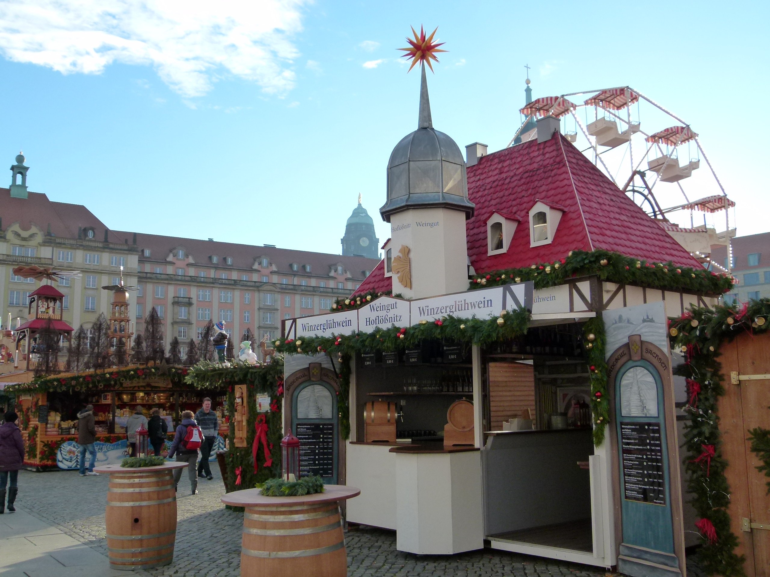 Ein geschäftiger Weihnachtsmarkt in Nürnberg, Deutschland mit Menschen um dekorierte Stände, festliche Lichter und Schmuck, Gebäude, ein Riesenrad und ein Schild auf der rechten Seite.