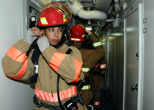 Feuerwehrleute in Uniform, die zusammen in einem Trainingsraum mit Rohren und Equipment im Hintergrund stehen.
