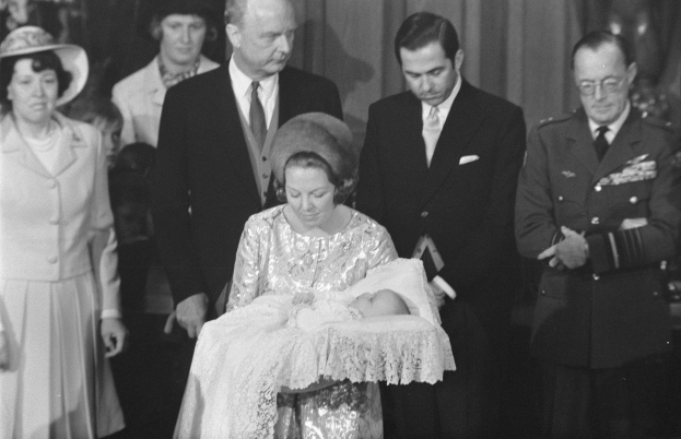 Königin Elizabeth II. wiegt ihren neugeborenen Sohn Prinz Philip, während Prinz Philip, Herzog von Edinburgh, neben ihnen in einem Anzug und einer Krawatte steht, mit Vorhängen im Hintergrund.