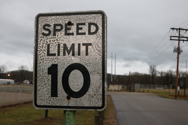Tempobegrenzungsschild am Straßenrand mit Gras, Strommasten, Häusern, Bäumen und einem bewölkten Himmel.