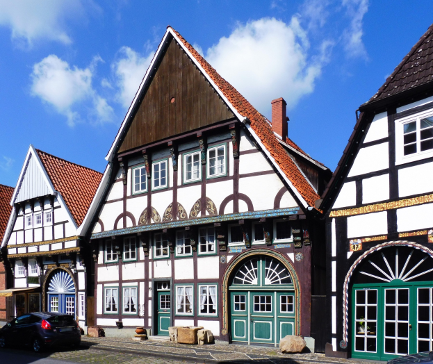 Reihe von Fachwerkhäusern mit Fenstern und Türen in der Altstadt von Heidelberg, mit Fahrzeugen auf der Straße und einer bewölkten Himmel im Hintergrund.