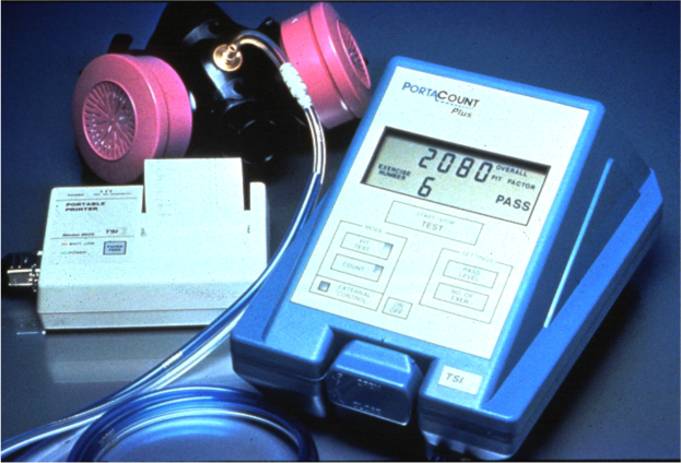 Eine Gasmaske auf einem Tisch neben einem elektronischen Gasdetektorgerät mit angeschlossenem Kabel.