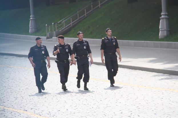 Drei Polizisten in Uniform auf einer Straße mit Pfählen, Geländern, Treppen und Gras im Hintergrund.