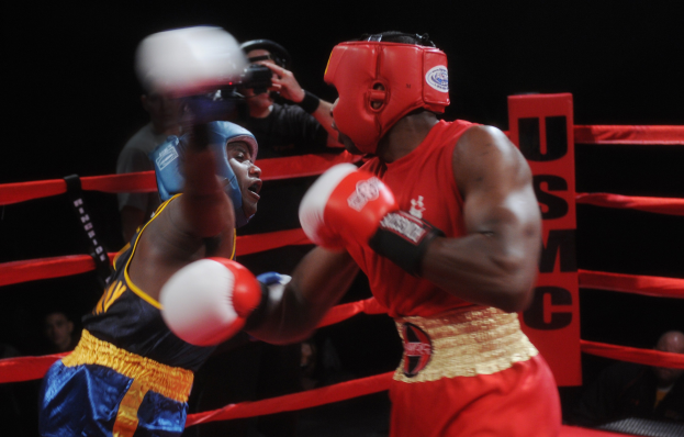 Zwei Boxer im Ring in einem Kampf, mit einem Fotografen und Zuschauern im Hintergrund bei dramatischer Beleuchtung.