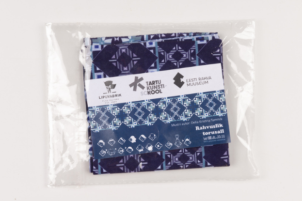 Ein blau-weiß gemustertes Stoffstück mit Etikett, Teil der Sammlung Tartu Kunsti Skool, liegt in einer Plastiktüte auf einer weißen Oberfläche.