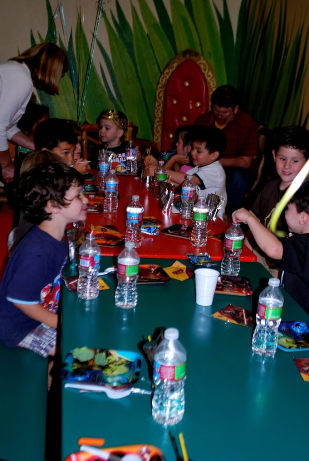 Eine Gruppe von Kindern sitzt um einen Tisch und genießt Snacks bei einer Geburtstagsfeier.