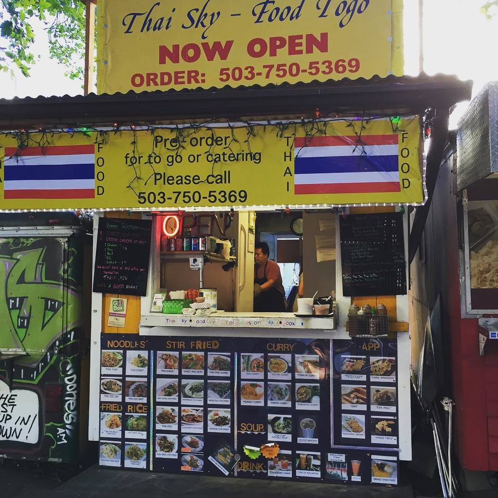 Läden, Getränkedosen, Speisekarten, eine Uhr, Gewürze in Plastikbehältern, Gewürze, Werbetafeln, Namensschilder und Himmel.