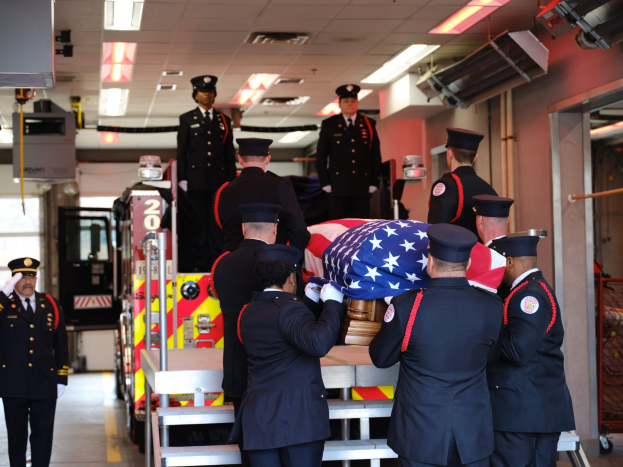 Gruppe uniformierter Männer, die einen Sarg tragen, der mit einer amerikanischen Flagge bedeckt ist, bei einer Beerdigungszeremonie.