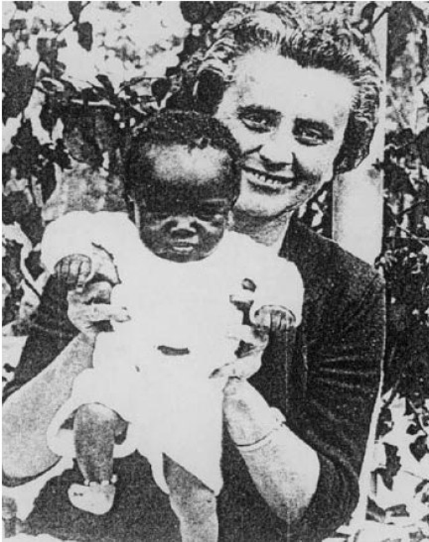 Ein Schwarz-Weiß-Foto einer Frau, die strahlend in die Kamera lächelt, während sie ein Baby hält, mit Blättern im Hintergrund.