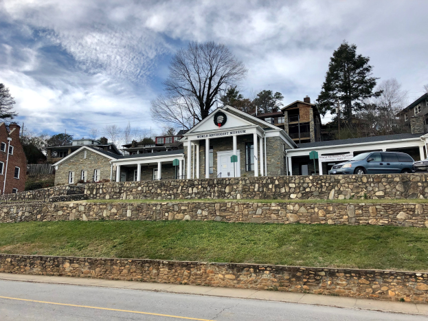 Steinwand mit parkenden Autos davor, umgeben von Gebäuden, Bäumen und einem bewölkten Himmel; das Weltkulturerbe-Museum, kürzlich wiedereröffnet.