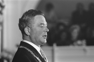 Ein Mann im Anzug und Krawatte steht an einem Rednerpult mit Mikrofon und spricht zu einer unscharfen Menge, der ein Politiker zu sein scheint.