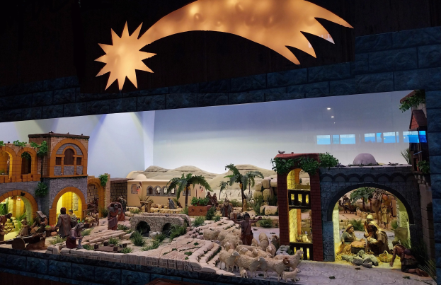 Eine Krippe mit beleuchteten Figuren, Tieren, Häusern und Pflanzen vor einer Wand.