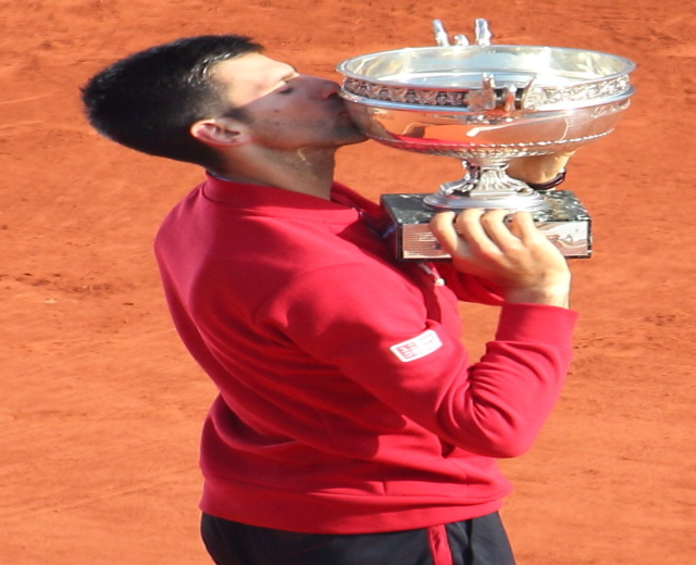 Novak Djokovic hält den French-Open-Pokal nach Sieg gegen Rafael Nadal in der Herren-Einzel-Finalrunde, steht mit triumphierendem Gesichtsausdruck da und küsst den Pokal.