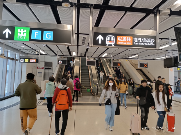 Menschen mit Gepäck durch einen geschlossenen Flughafen: Rolltreppen, Infotafeln, Deckenleuchten und Glaswände im Hintergrund.