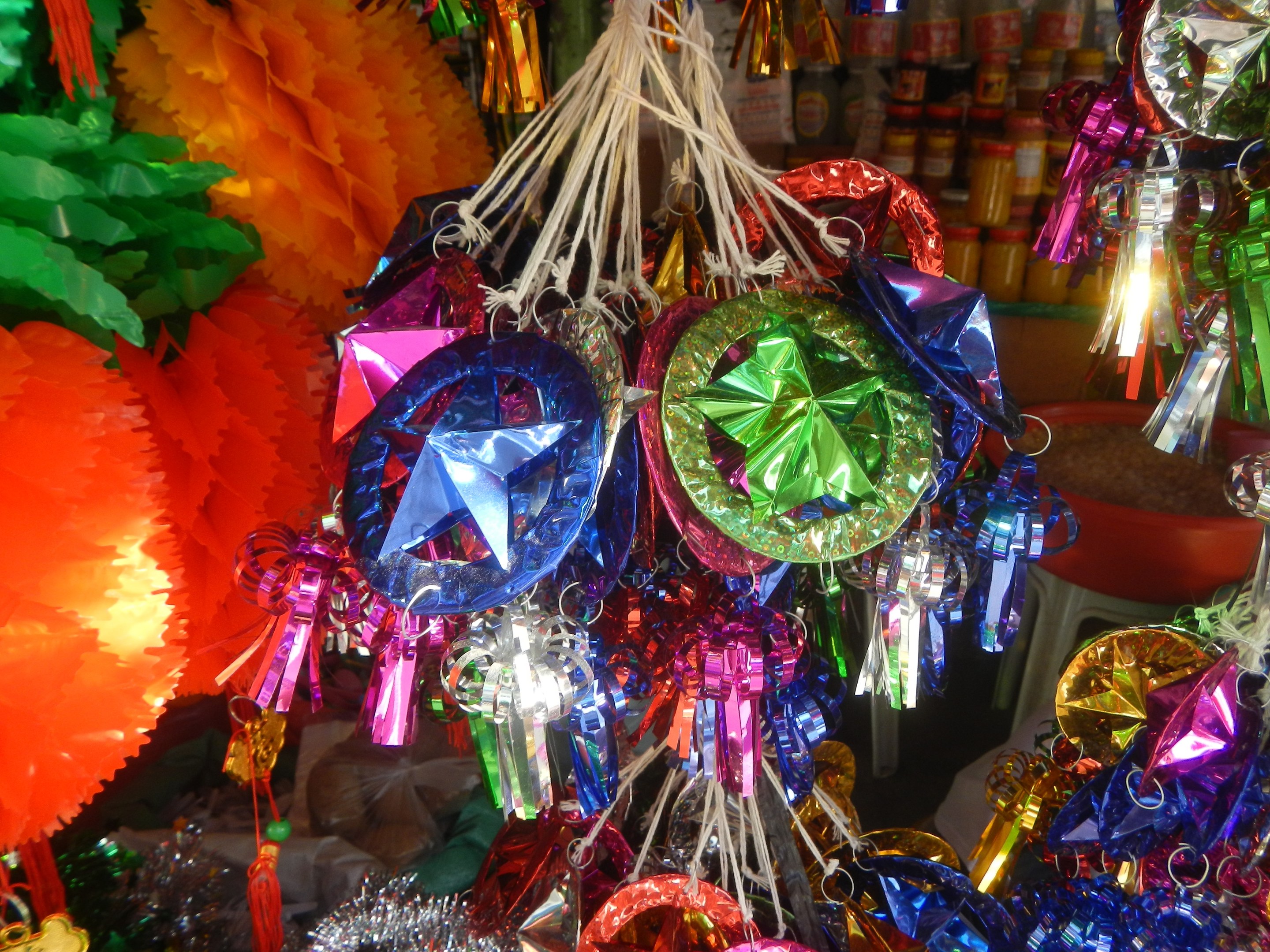 Bunte Festschmuckdekorationen, darunter Laternen und Bänder, hängen von der Decke über Regalen mit Flaschen im Hintergrund.