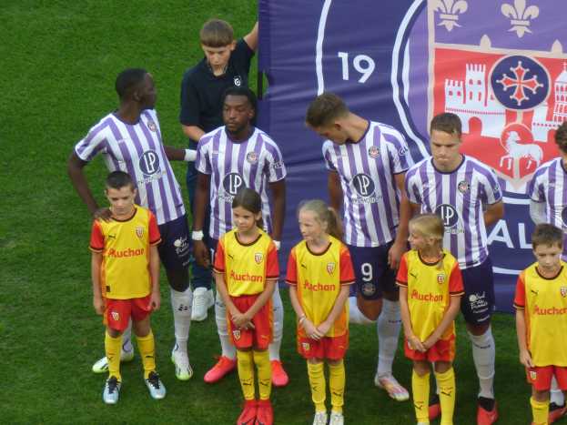 Gruppe junger Fußballspieler auf einem grünen Feld mit einem "Ligue 1"-Plakat im Hintergrund.