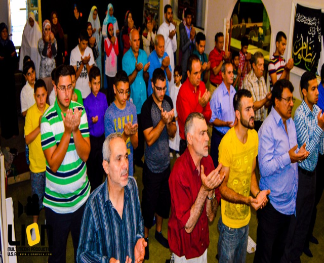 Menschen beten in einem Saal mit Text in der linken unteren Ecke.