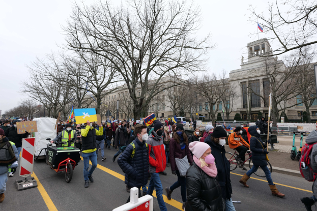 Eine große Protestmarsch mit Menschen, die eine Straße in Washington, D.C. entlanggehen, einige halten Schilder und andere fahren Fahrräder, mit Bäumen und einem Gebäude im Hintergrund unter einem klaren blauen Himmel am 21. Januar 2020.