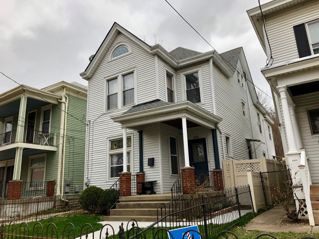 Reihe von Häusern mit Fenstern, Türen, Säulen, Geländern, Treppen und Dächern, umgeben von einem Metallzaun, Gras, Pflanzen, Bäumen und einem bewölkten Himmel; Mietschild unten mit der Adresse 5901 S Elmwood Ave, Chicago 60618.