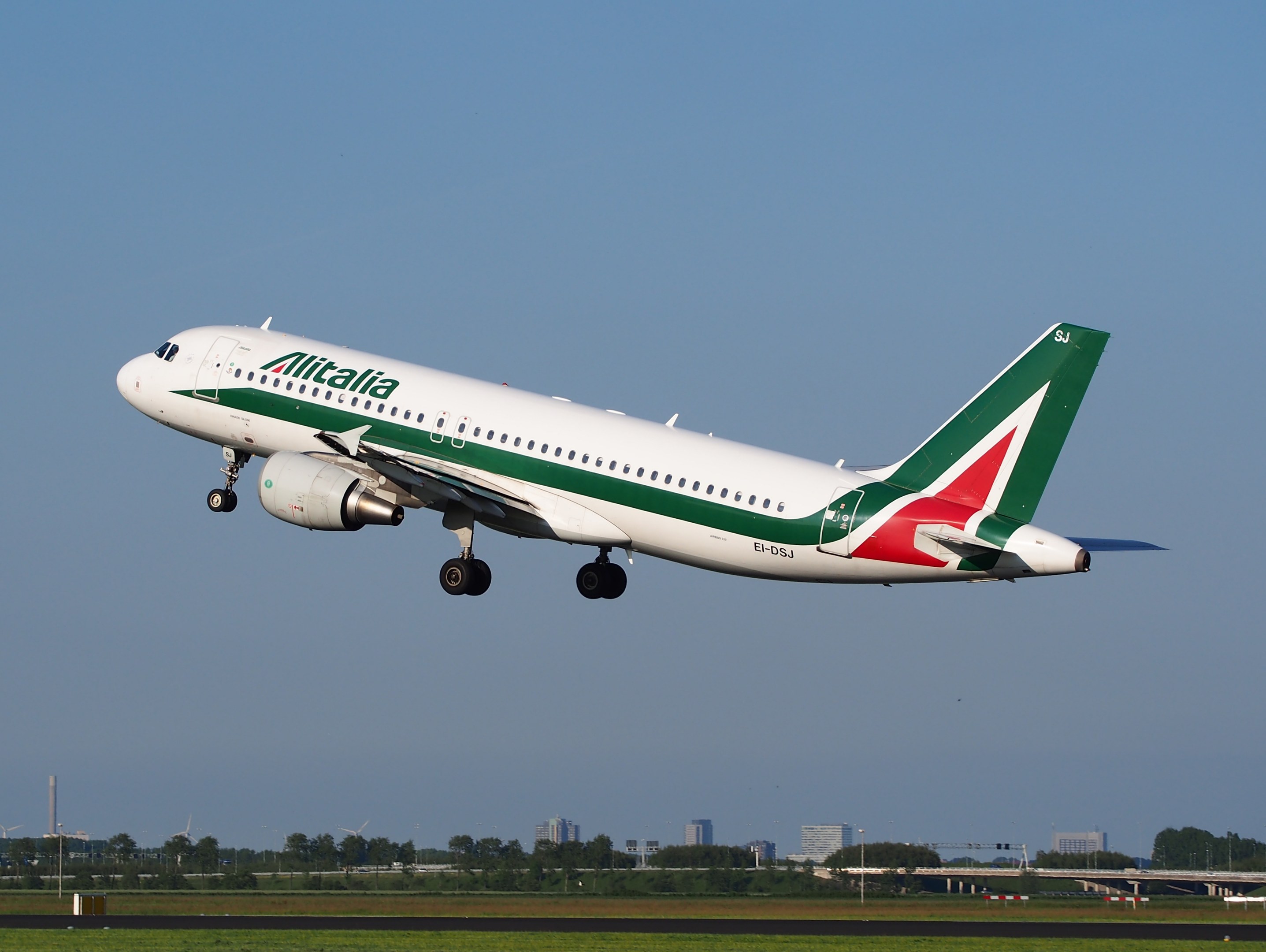 Alitalia Airbus A320-232 ERJ-EJZ Flugzeug beim Starten vom Frankfurt Airport mit grünem Gras, Bäumen, Gebäuden und einem klaren blauen Himmel im Hintergrund.