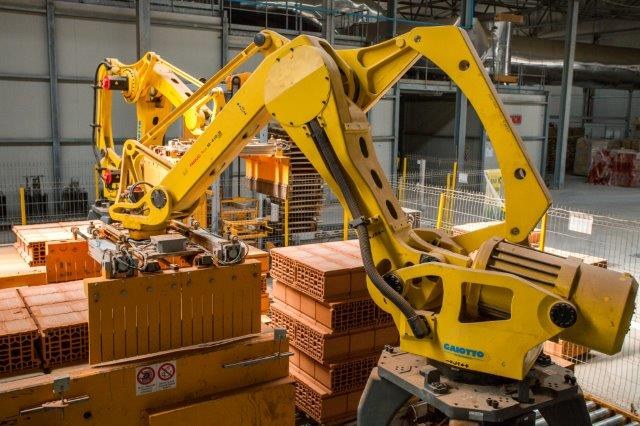 Großes Industriegelände mit gestapelten Kisten, Kränen, Zäunen, Strommasten und einer fernen Begrenzungsmauer.