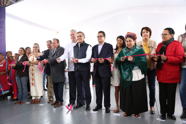 Gruppe von Menschen bei einer Scherenschnitte-Zeremonie mit Papieren auf dem Boden und einem weißen Tuch im Hintergrund.