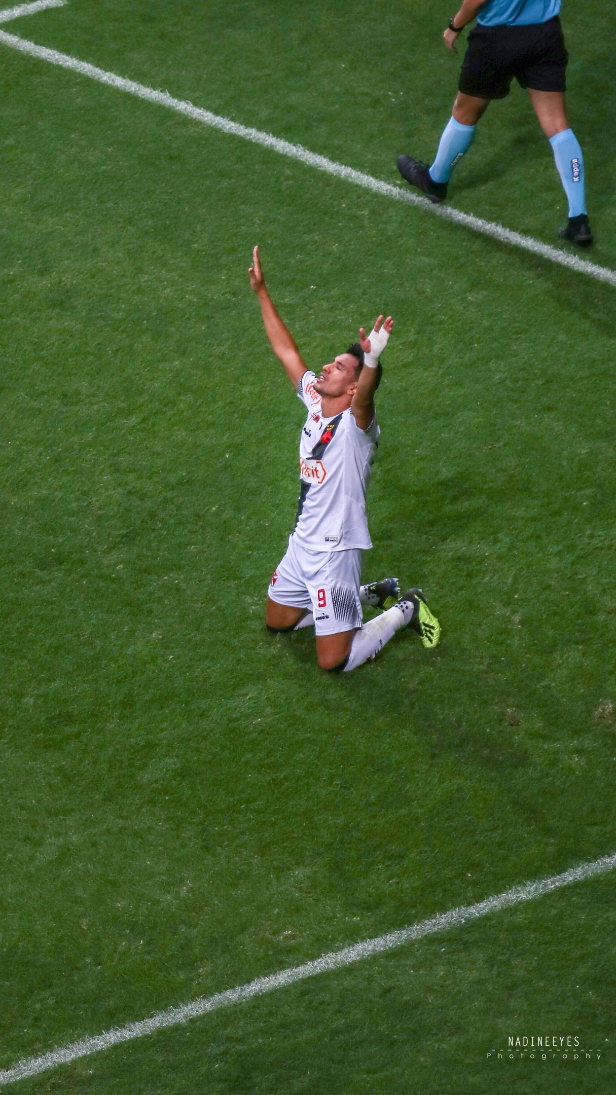 Ein Fußballspieler in Uniform kniet auf dem Feld und streckt die Arme aus.