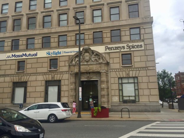 Großes Gebäude mit parkenden Autos, Straßenlaternen, Lichtern, fahrenden Fahrzeugen, Fußgängern, Grünflächen und bewölktem Himmel, als Massachusetts Mutual Financial Group Hauptsitz identifiziert.