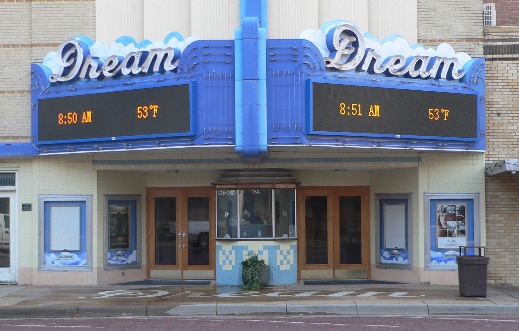Außenansicht des Dream Theaters in St. Louis, Missouri mit Glastüren und -fenstern, einem Namen-Schild, einem Mülleimer, einer Topfpflanze und einer Straße unten.