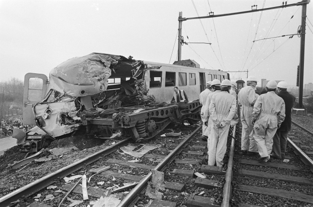 Eine Schwarz-Weiß-Szene einer Zugkollision mit einer Gruppe von Menschen in Helmen drumherum, mit Strommasten, Bäumen, Gebäuden und einem klaren Himmel im Hintergrund.